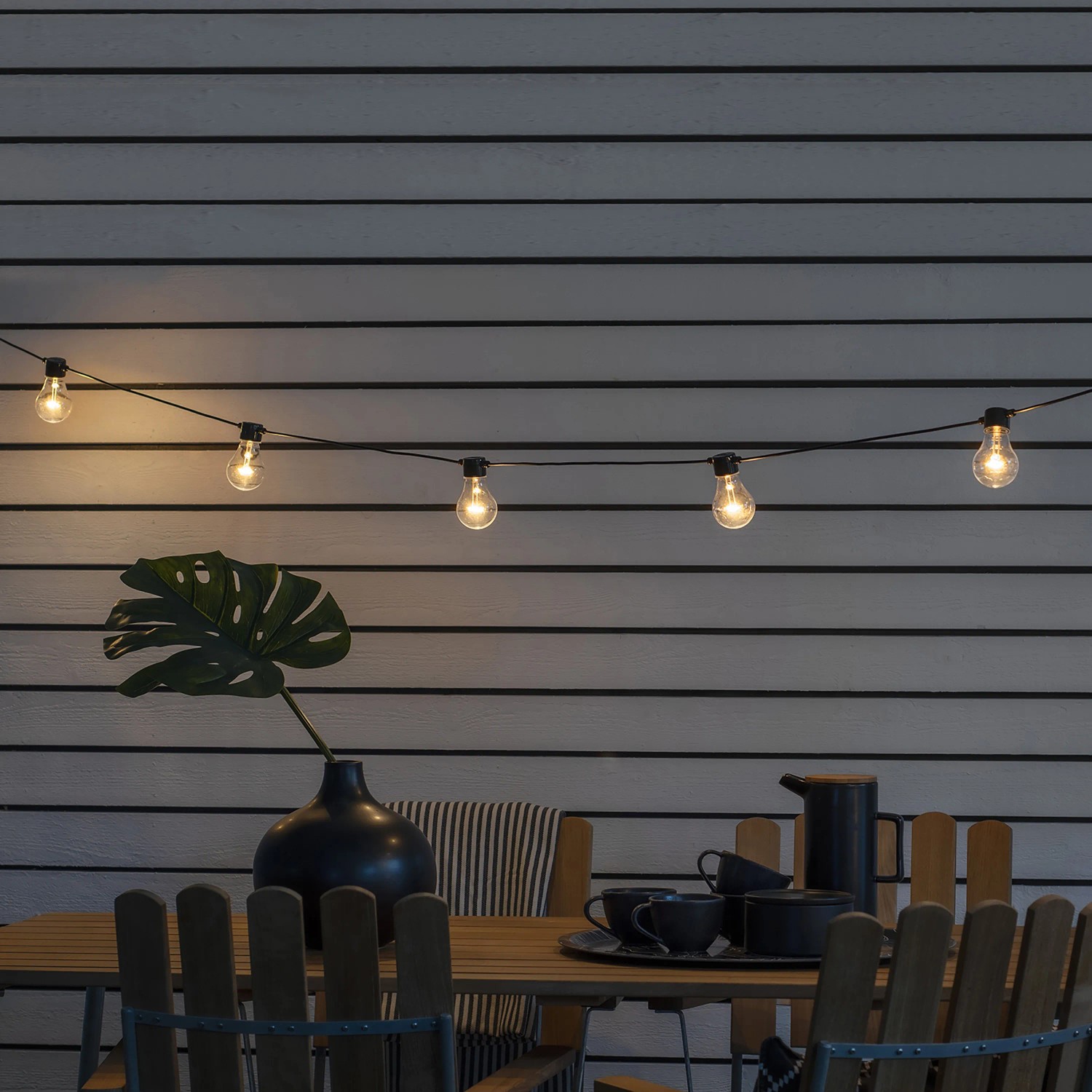 Konstsmide LED Biergarten Lichterkette mit 10 bernsteinfarbenen Leuchtmitteln über einem Gartentisch.