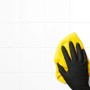 Hand mit schwarzem, latexfreiem Einmalhandschuh reinigt weiße Fliesen mit gelbem Tuch.