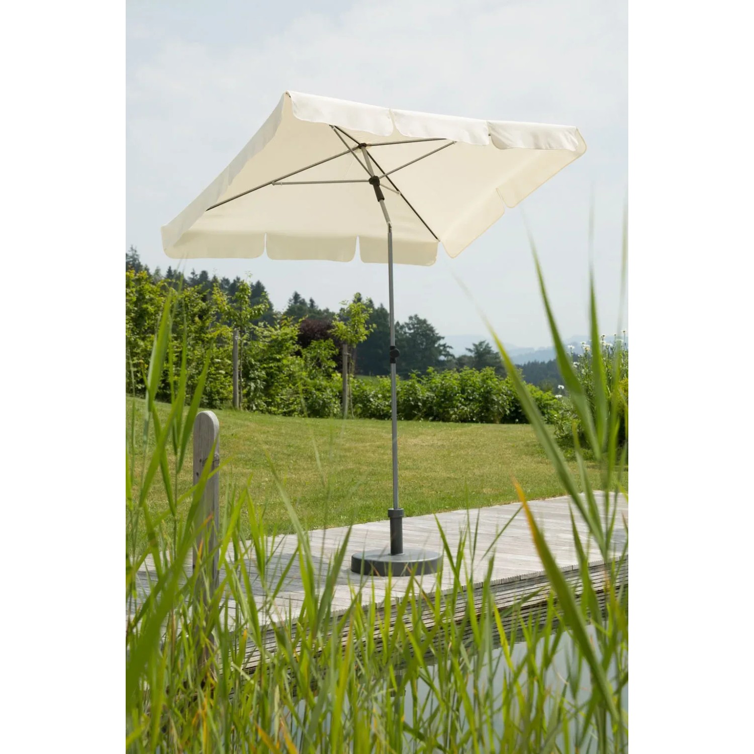 Rechteckiger, naturfarbener Schneider Balkonschirm Locarno mit Push-Up Mechanik auf Terrasse mit Grün.