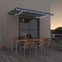 vidaXL Markise, blau-weiß gestreift, mit LED-Beleuchtung über einer Terrasse mit Tisch und Stühlen.