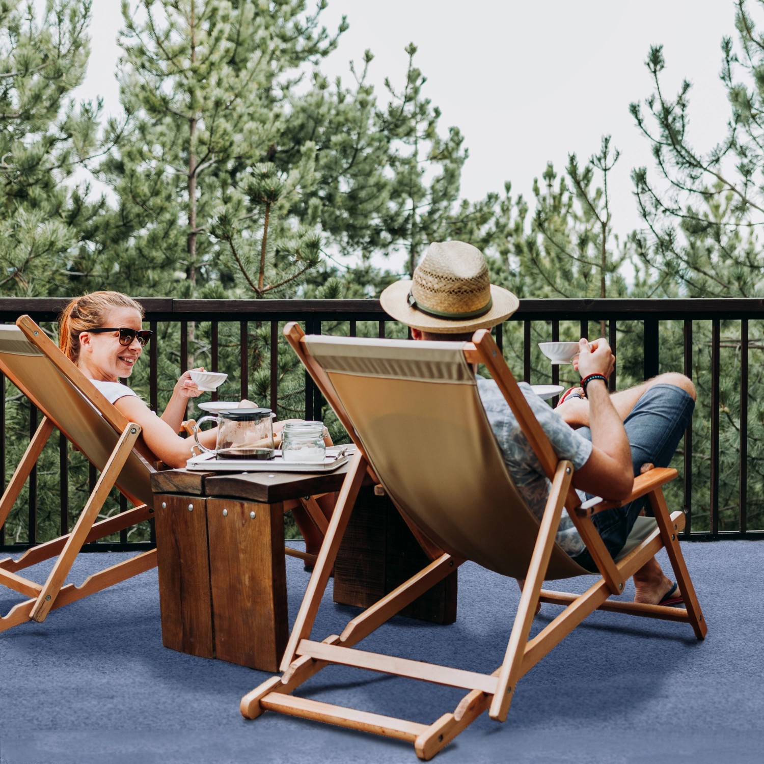 Blauer Primaflor Rasenteppich auf Terrasse mit entspannten Personen in Liegestühlen.