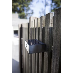 Moderne Lutec LED Solar-Wandleuchte Brick aus Edelstahl an Holzzaun, eckig, mit Bewegungsmelder.
