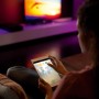 Frau steuert Philips Hue Lightstrip Plus mit Tablet, indirekte Beleuchtung im Wohnzimmer.