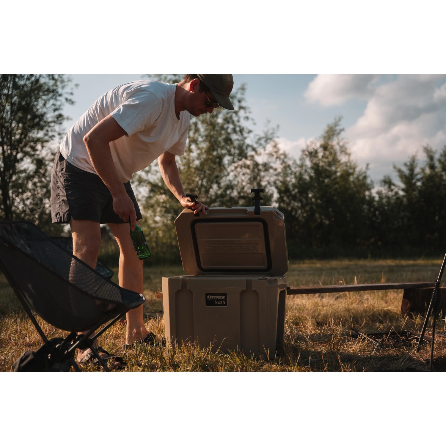Petromax Kühlbox 25 l in Sand mit Person beim Öffnen im Outdoor-Einsatz.