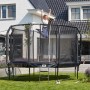 Schwarzes Salta Trampolin First Class ø 305 cm mit Sicherheitsnetz und Leiter im Garten.