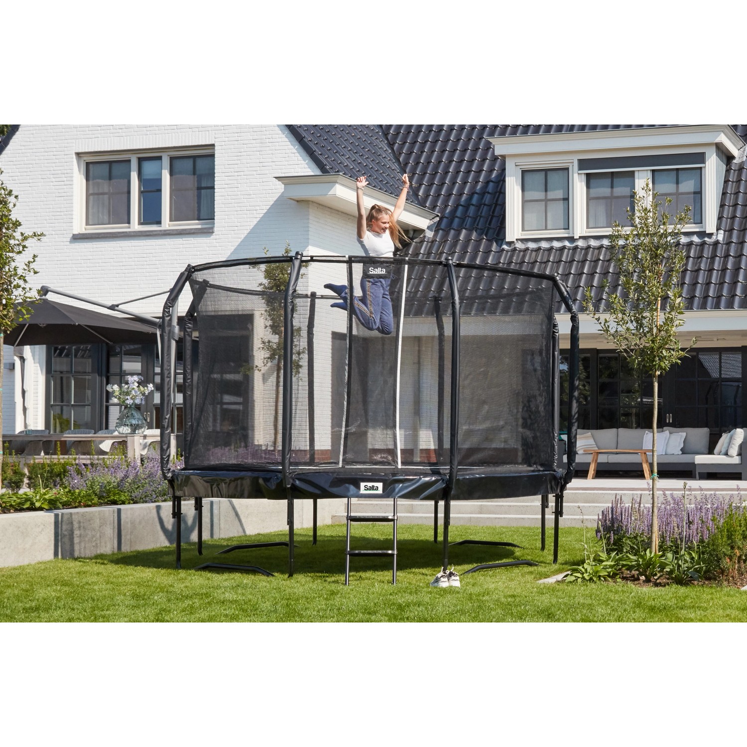Schwarzes Salta Trampolin First Class ø 305 cm mit Sicherheitsnetz und Leiter im Garten.