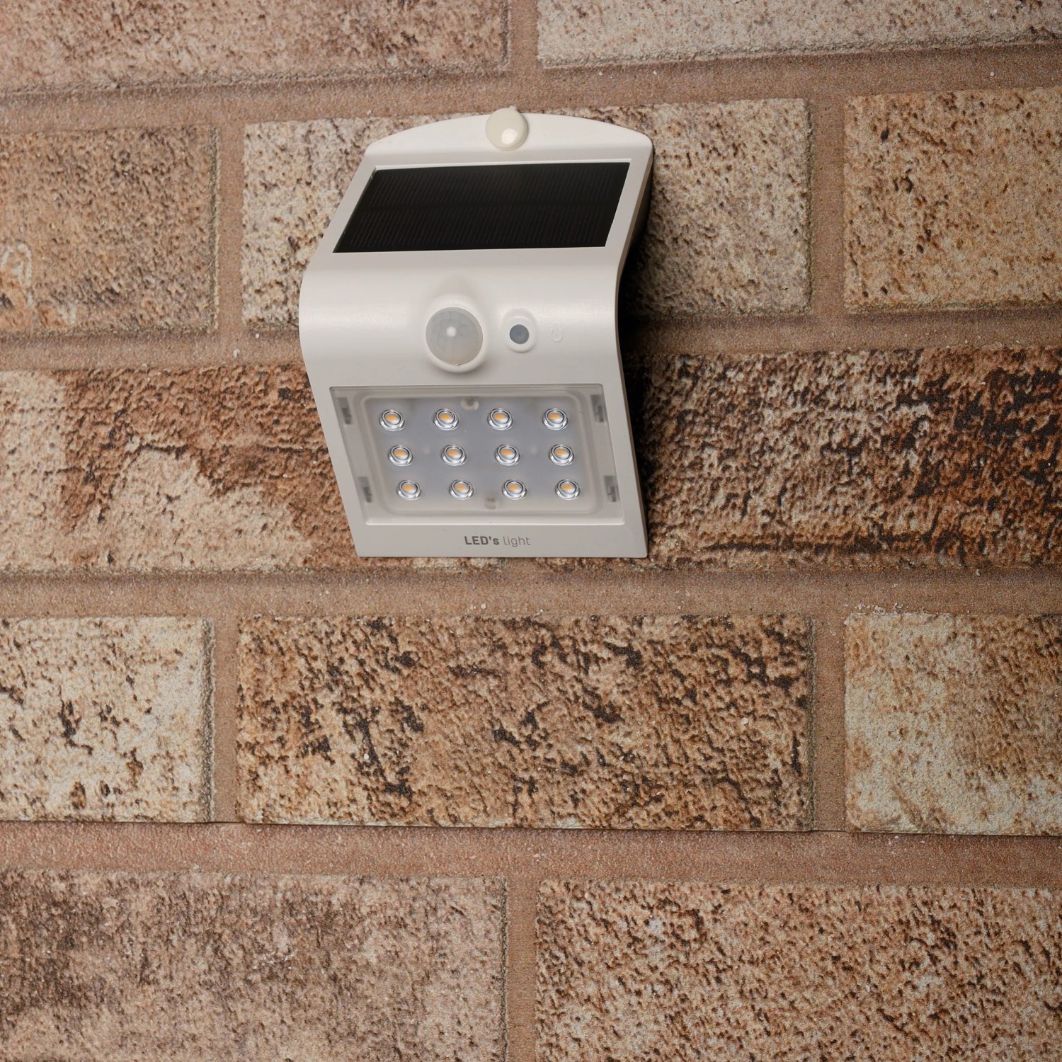 Weiße LED Solar-Außenleuchte mit Sensor an einer Backsteinwand. Flutlicht mit 220 Lumen.