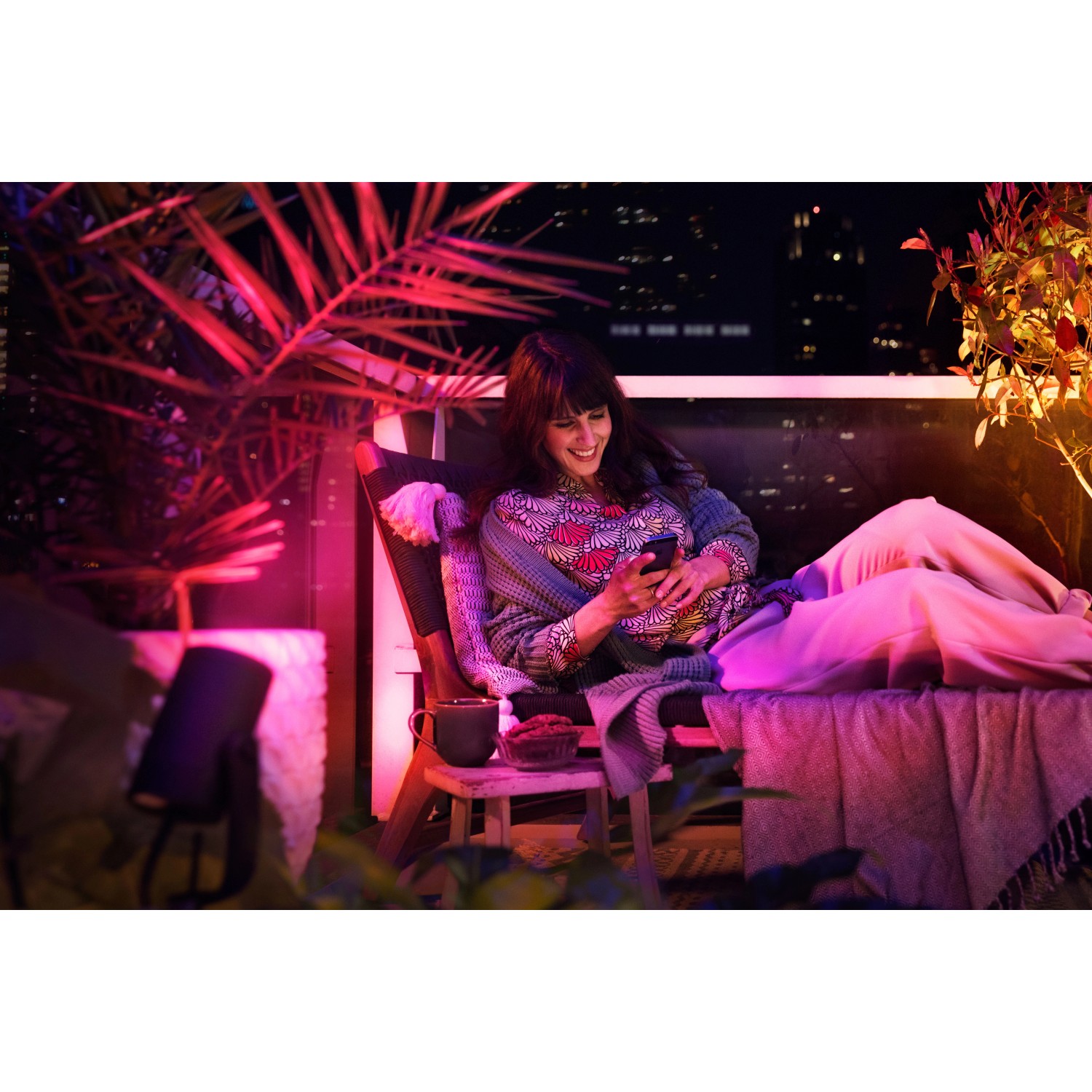 Frau entspannt im Garten, beleuchtet mit Philips Hue Lily LED-Spot in Farbe. Smarte Gartenbeleuchtung.