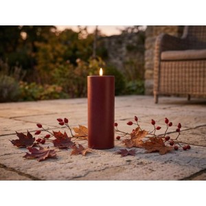 Bordeauxfarbene LED-Outdoor-Kerze Niumi (Ø 8x20cm) mit flackerndem Licht auf Terrasse, umgeben von Herbstlaub.