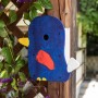 Bemalter Nistkasten-Bausatz Self-Made in Vogelform am Holzpfosten mit Pflanzen.