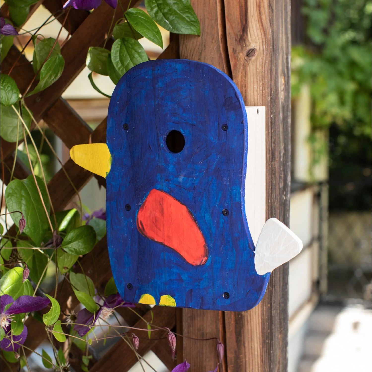 Bemalter Nistkasten-Bausatz Self-Made in Vogelform am Holzpfosten mit Pflanzen.