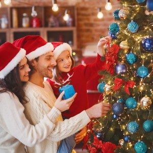 Fröhliche Familie schmückt Weihnachtsbaum mit petrolfarbenen Weihnachtskugeln. Bruchsicherer Christbaumschmuck aus Kunststoff.