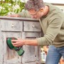 Mann schleift alte Holzkommode mit grünem Bosch Akku-Multischleifer. Vielseitige Schleifmaschine für Holz & Möbel.