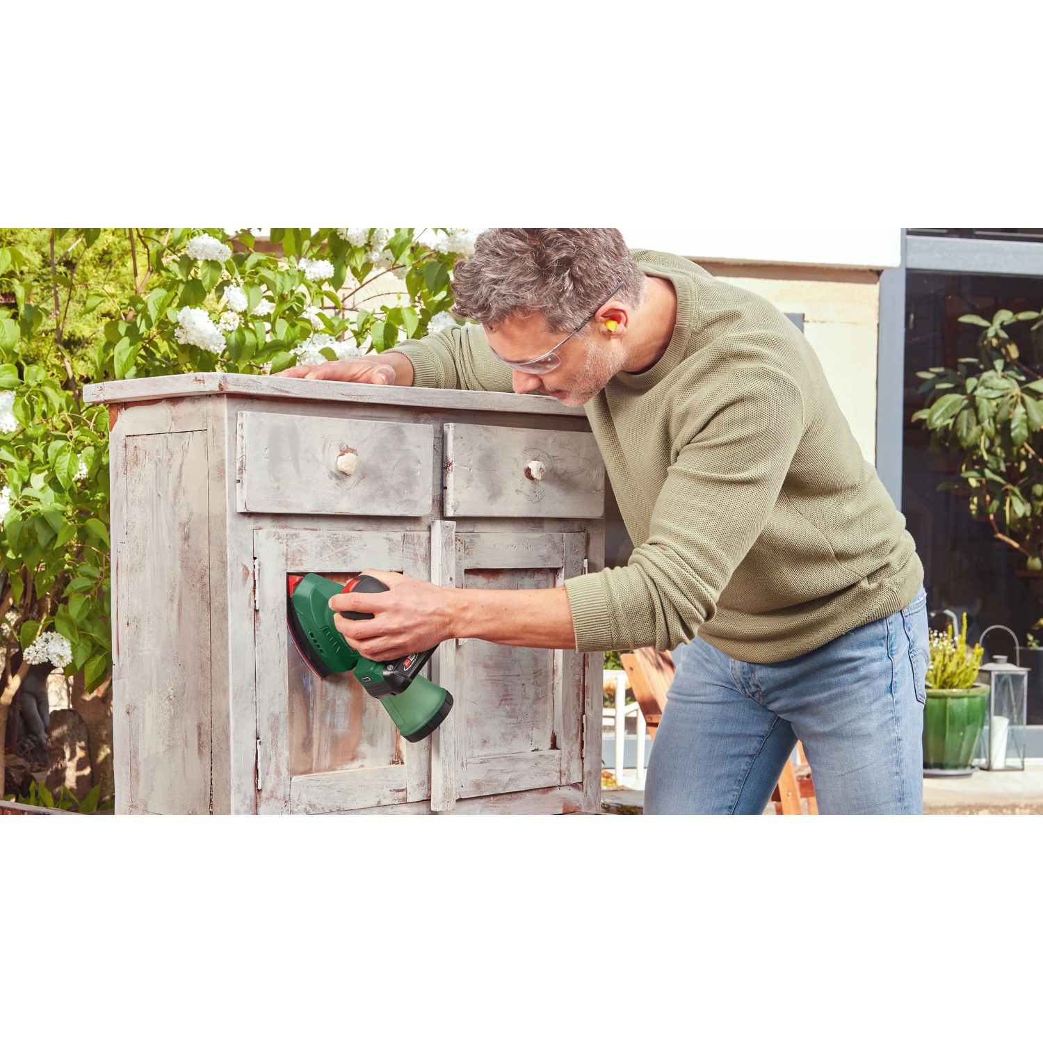 Mann schleift alte Holzkommode mit grünem Bosch Akku-Multischleifer. Vielseitige Schleifmaschine für Holz & Möbel.