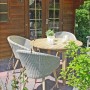 Runder Gartentisch Arvada Natur Ø 110 cm mit Stühlen auf Terrasse vor Holzhütte.