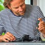 Mann repariert Gerät mit Bosch Präzisionsschraubendreher-Set. Schraubenzieher und Zubehör auf Tisch.