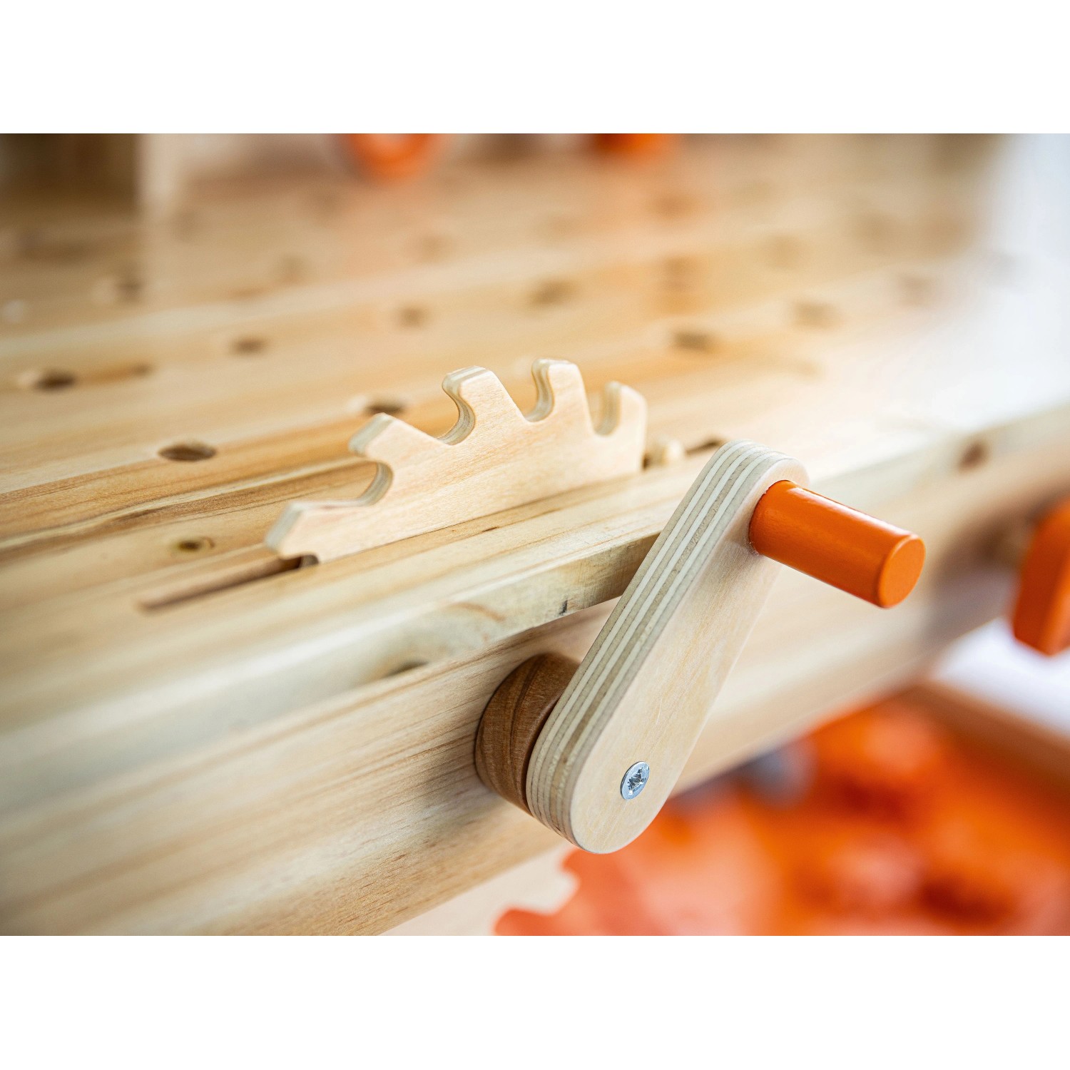 Nahaufnahme einer OBI Kinderwerkbank aus Holz mit Spielzeug-Säge und orangefarbener Kurbel.