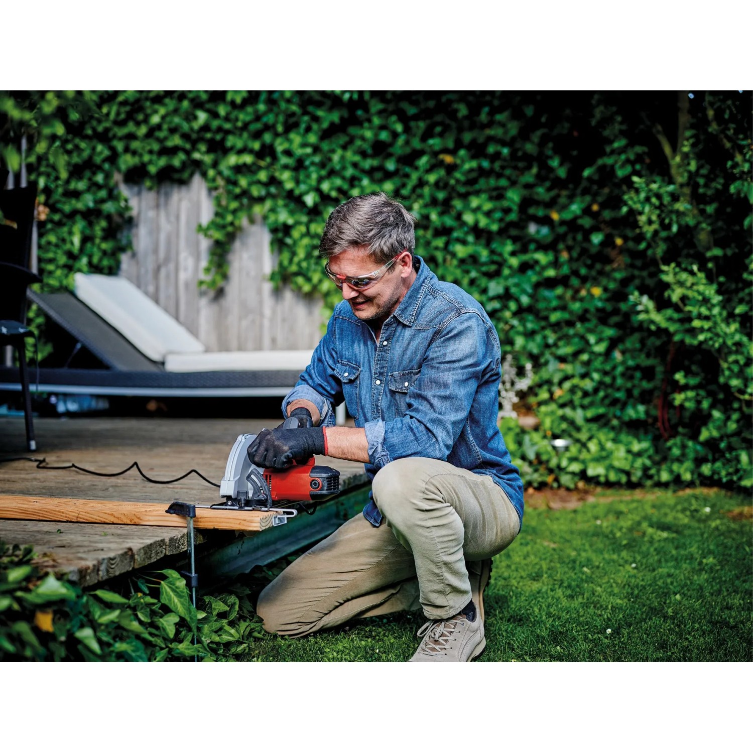 Mann sägt Holz mit der roten Einhell Handkreissäge TC-CS 1250 im Garten.