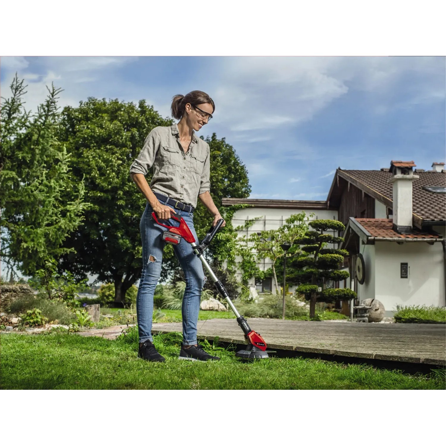 Frau trimmt Rasen mit dem roten Einhell Akku-Rasentrimmer GE-CT 18 Li Kit Power X-Change.