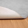 Grauer runder Kunstfell Teppich aus Polyester, weich, mit sichtbarer rutschfester Unterseite auf Holz.
