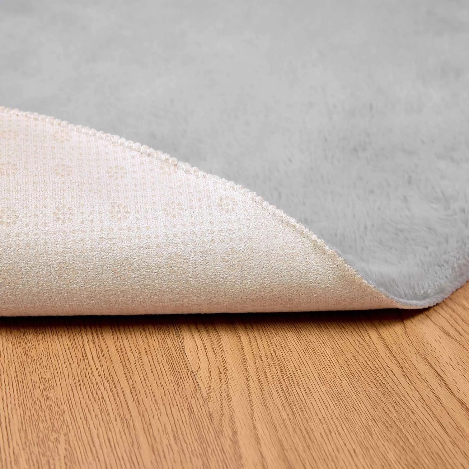 Grauer runder Kunstfell Teppich aus Polyester, weich, mit sichtbarer rutschfester Unterseite auf Holz.
