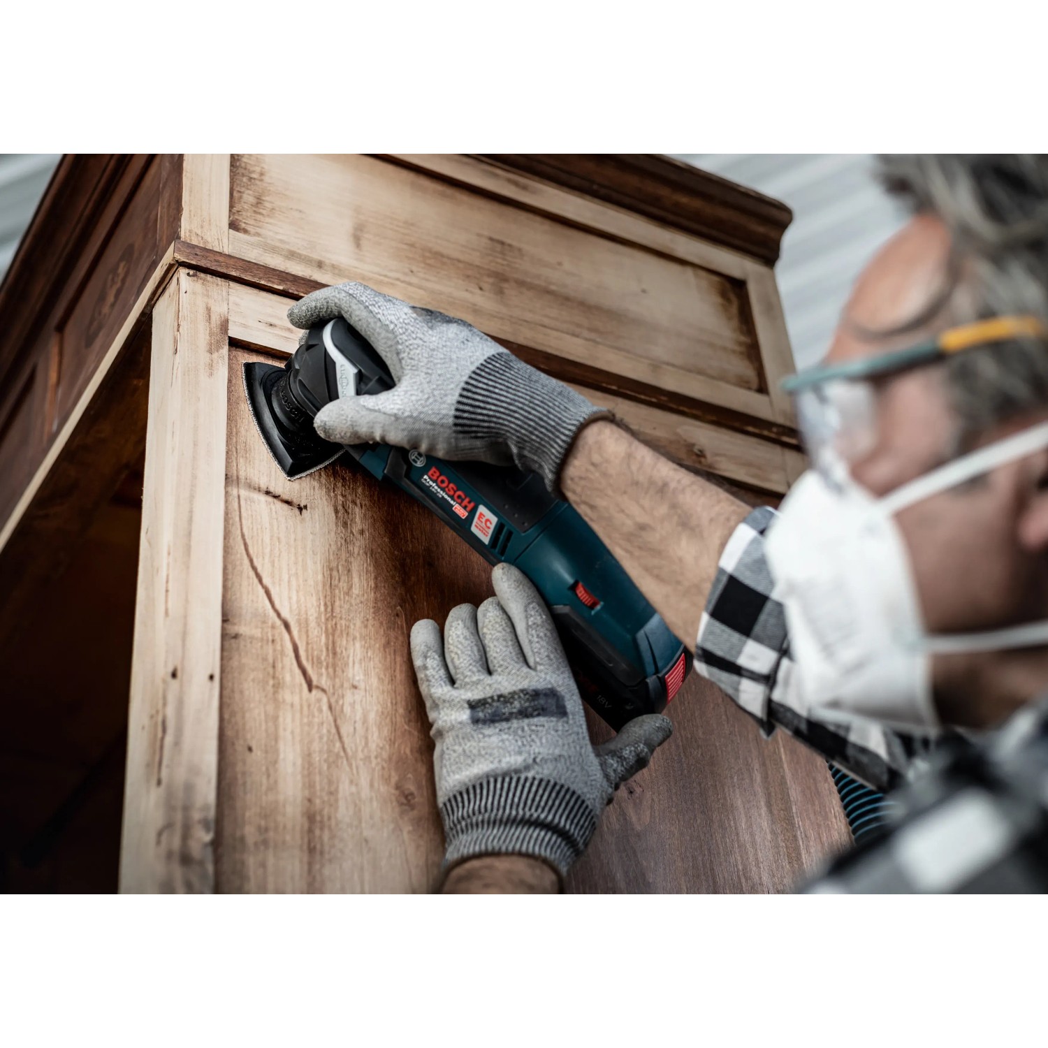 Mann schleift Holzschrank mit Bosch Deltaschleifer und Schleifblatt C470 K100.