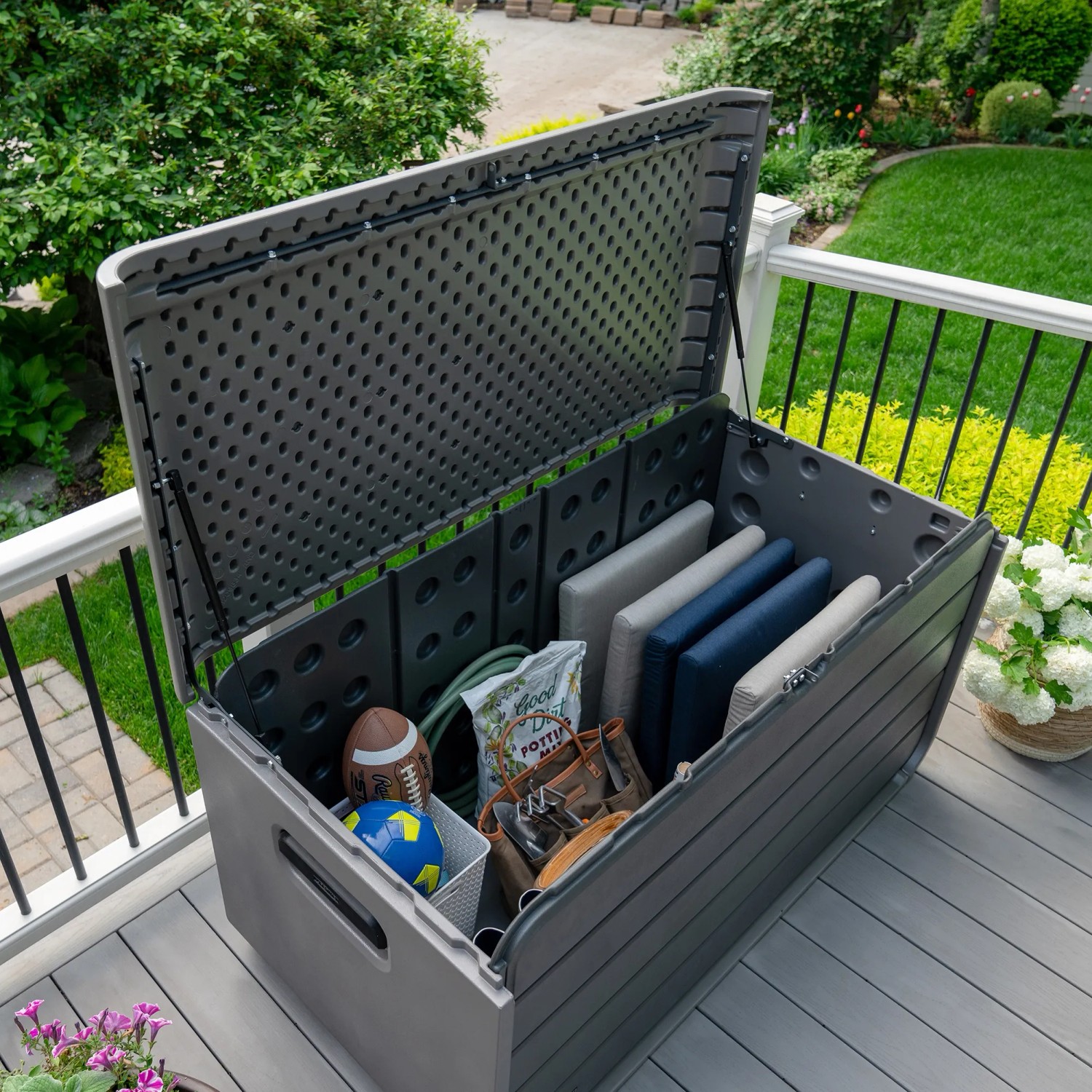 Geöffnete graue Lifetime Kissenbox 625 l mit Kissen und Spielzeug auf der Terrasse.