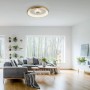 LED-Deckenleuchte Vertigo in Messing Matt (Ø 61,5 cm) im Wohnraum mit Sofa und Fenster.