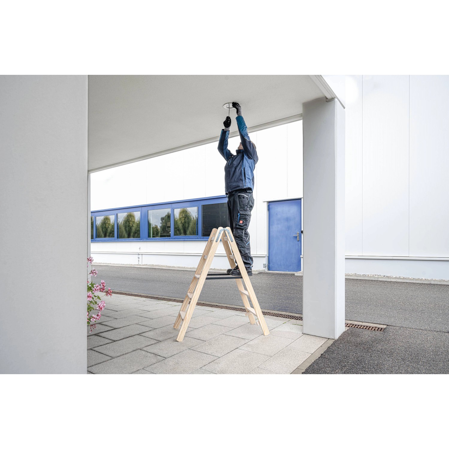 Mann auf PROREGAL Holz Stufen-Stehleiter (2x3 Stufen) bei Montagearbeiten.