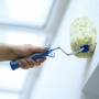 Hand streicht Wand mit LUX Polyamid Farbroller (25cm, blau/schwarz) für strukturierte Flächen.