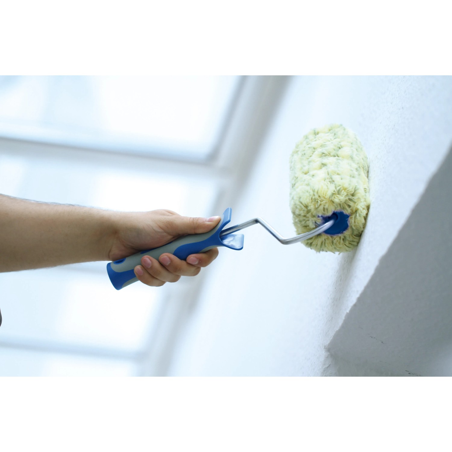 Hand streicht Wand mit LUX Polyamid Farbroller (25cm, blau/schwarz) für strukturierte Flächen.