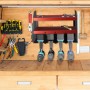 Rotes Stahl Werkzeugregal mit 2 Ablagen und 4 Haltern für Akkuschrauber an Holzwand. Organisiert Werkzeuge in der Werkstatt.