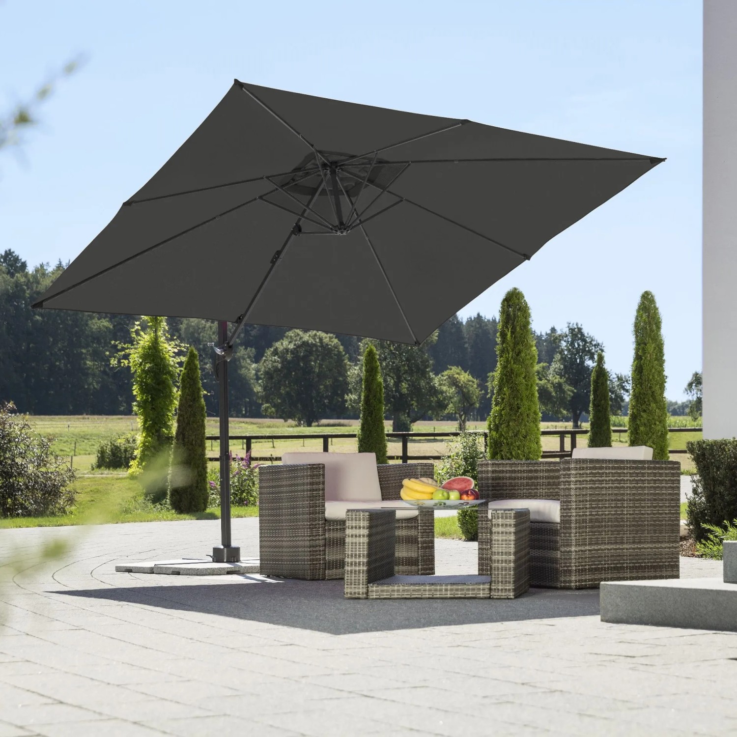 Quadratischer, anthrazitfarbener Schneider Ampelschirm Rhodos Junior 270x270 cm über einer Sitzgruppe im Garten.