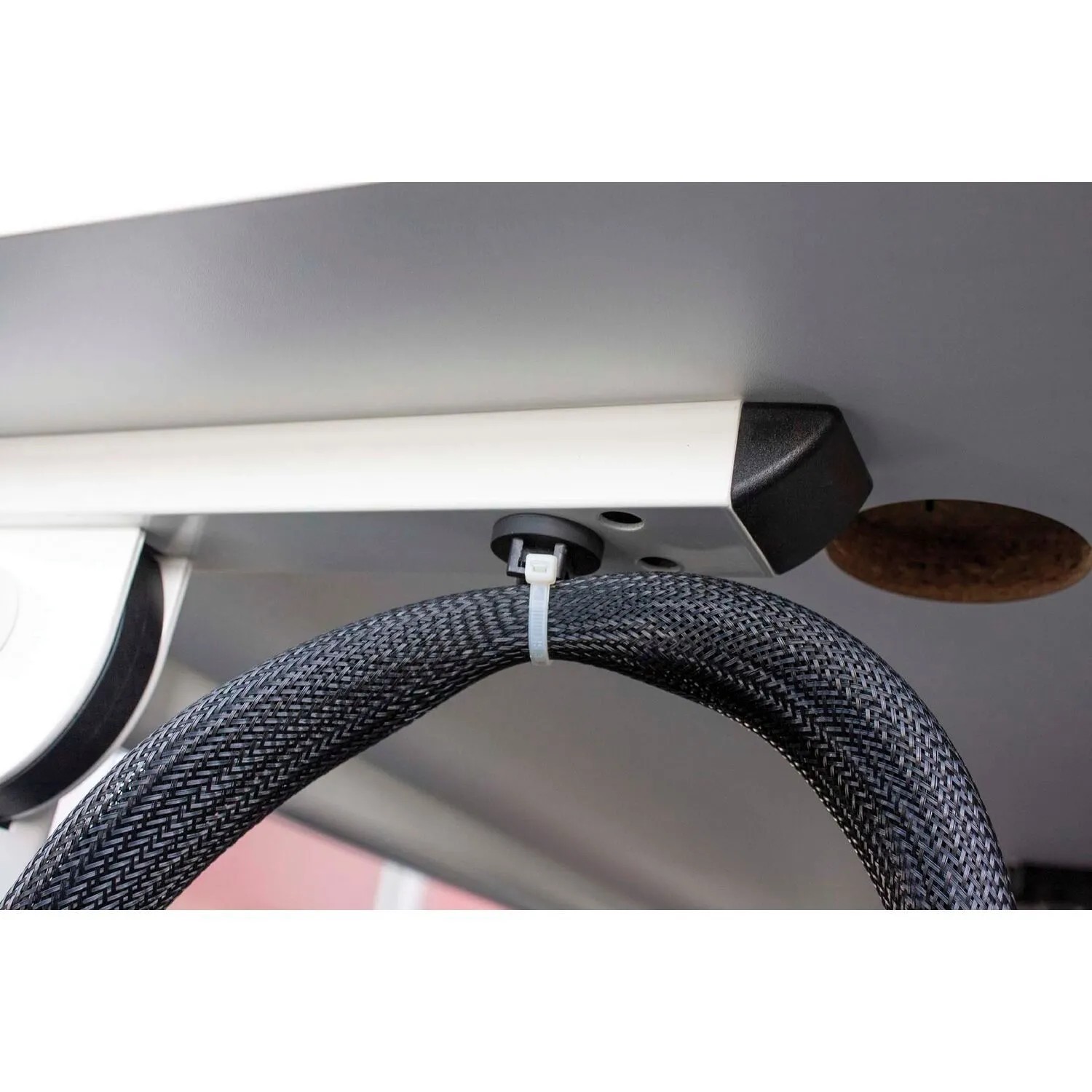 Schwarzer, flexibler EVOline Texflex Kabelschlauch mit Zipp, unter Schreibtisch für Kabelmanagement befestigt.