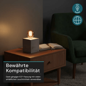 Graue LUXULA Tischleuchte mit E27 Fassung auf Nachttisch mit Buch und Sessel.