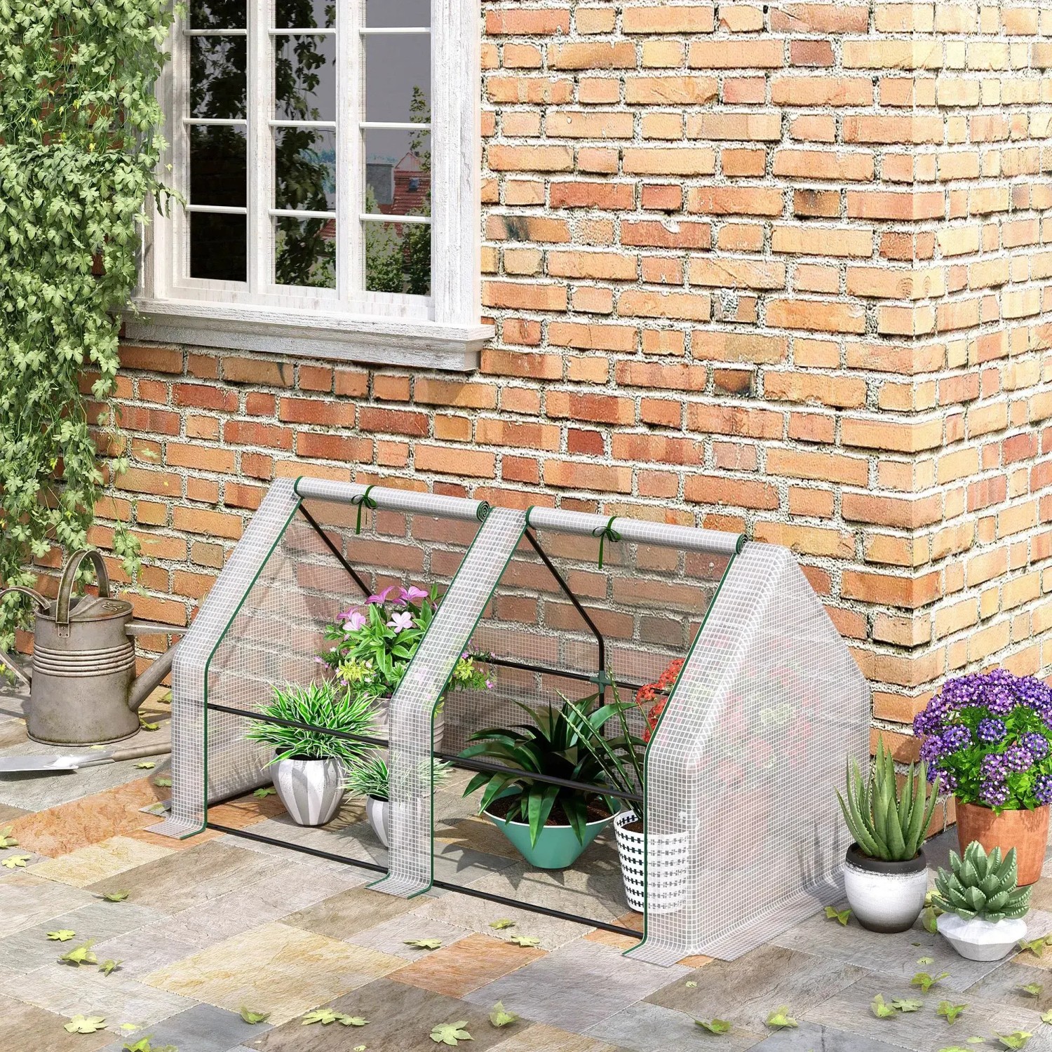Weißes Outsunny Gewächshaus mit Rollfenster und Pflanzen vor einer Backsteinmauer.