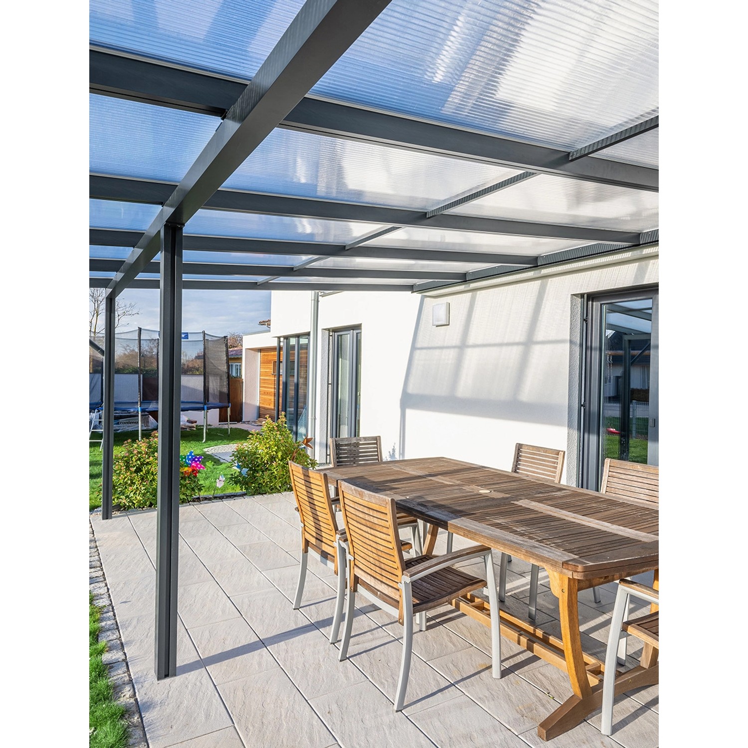 Gutta Terrassendach Premium Anthrazit mit Stegplatten, Esstisch und Gartenmöbel auf Terrasse.