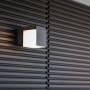 Moderne Lutec LED-Außenwandleuchte Cuba in Anthrazit mit warmweißem Licht an dunkler Holzwand.