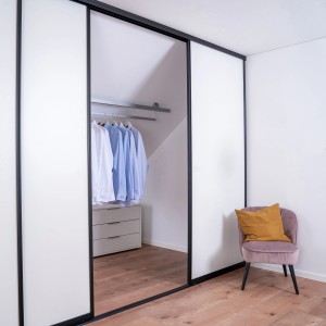 Schiebetür-Baupaket mit schwarzem Profil und weißer Tür, integriert in begehbaren Kleiderschrank.