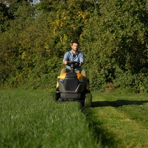 Gelber Stiga Rasentraktor Estate 598 W mit Mann beim Rasenmähen auf einer Wiese.