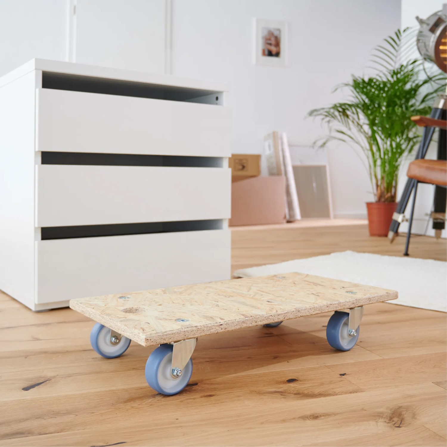 Wagner Transporthilfe mit OSB-Platte und blauen Rollen vor Kommode. Tragkraft 250 kg.