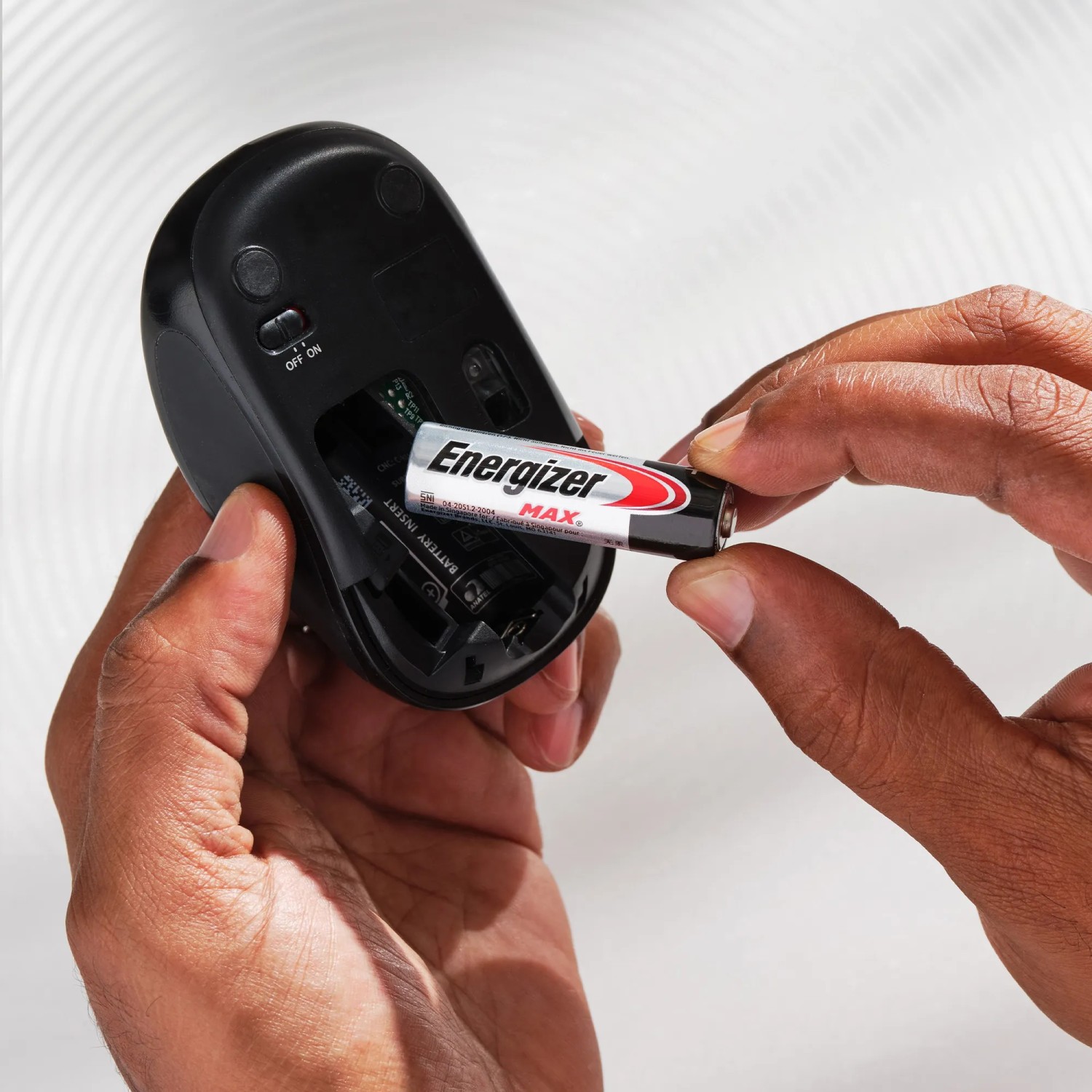 Einsetzen einer Energizer Max AA Batterie in eine schwarze Computermaus.