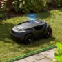 Schwarzer Mähroboter auf Rasen, blaues Signal. Grünes Begrenzungskabel am Wegrand für präzise Rasenpflege.