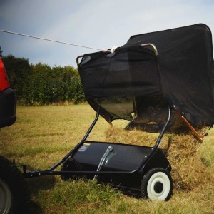 Schwarze Wiltec Rasenkehrmaschine, 96 cm Kehrbreite, an Aufsitzmäher gekoppelt, entleert Gras auf Rasen.