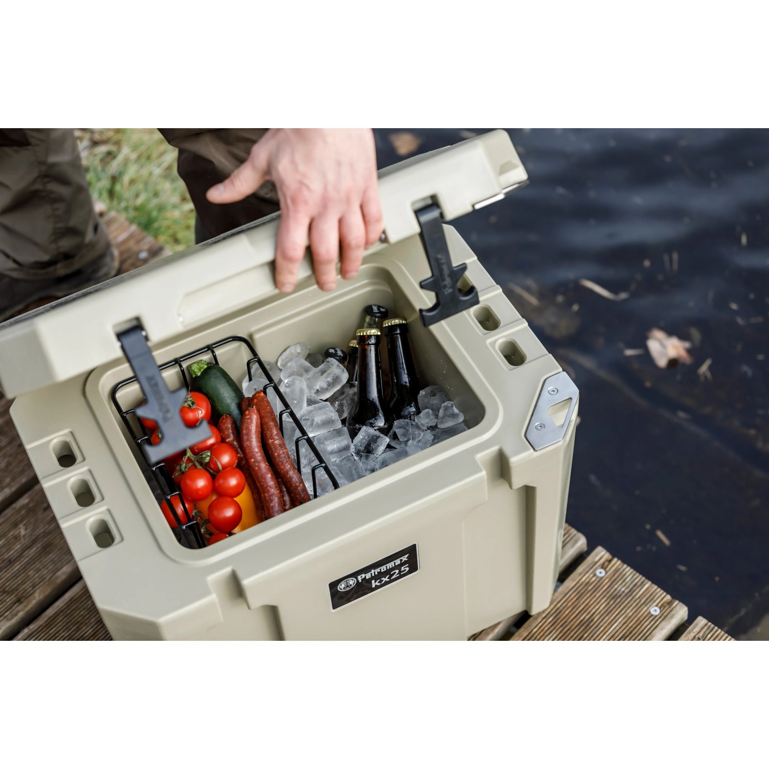 Geöffnete Petromax Kühlbox kx25 in Sand, gefüllt mit Eis, Getränken und Lebensmitteln.