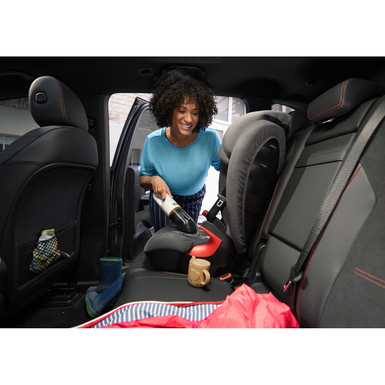 Frau saugt mit Kärcher Akku-Handstaubsauger CVH 2 einen Kindersitz im Auto.