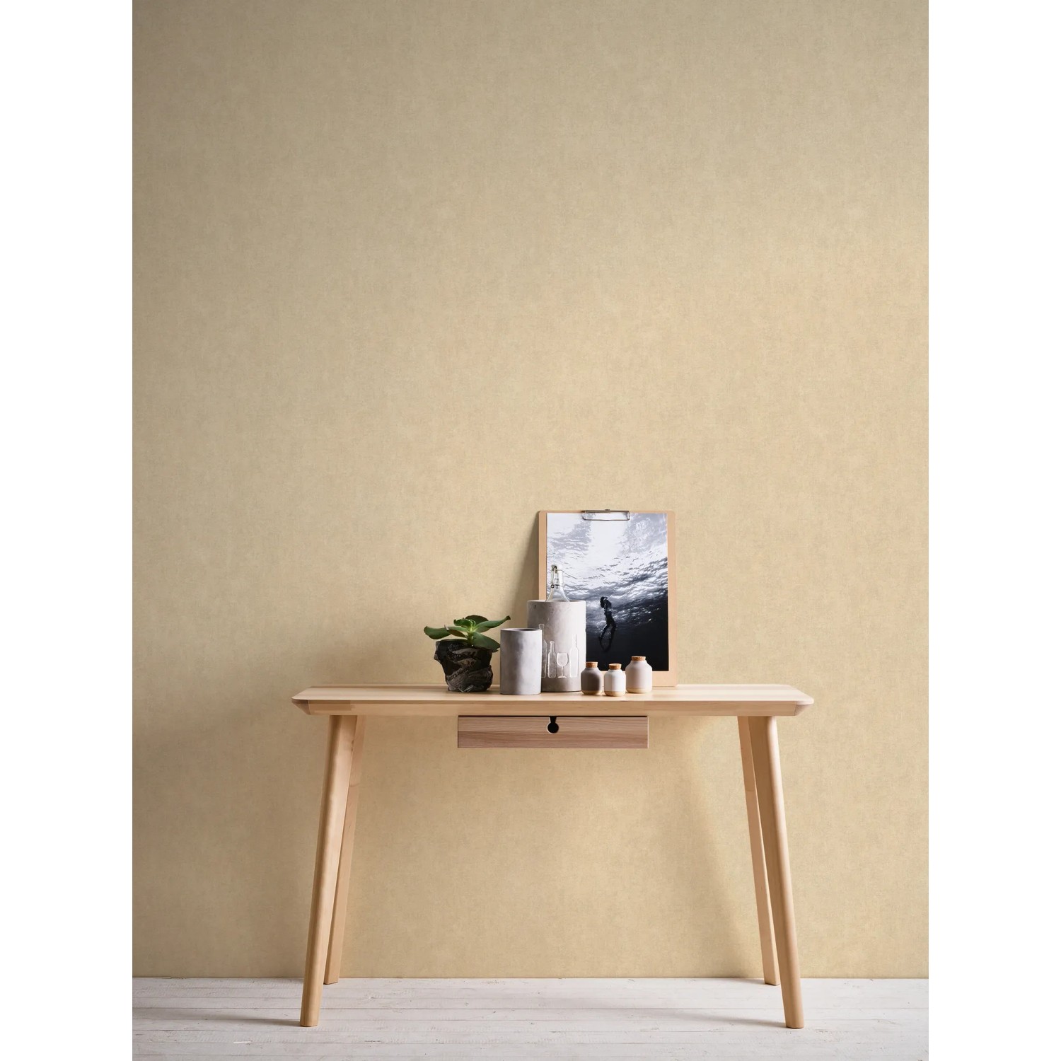 Beige-gelbe, matte Vliestapete Uni Glatt FSC® an Wand hinter Tisch mit Deko.