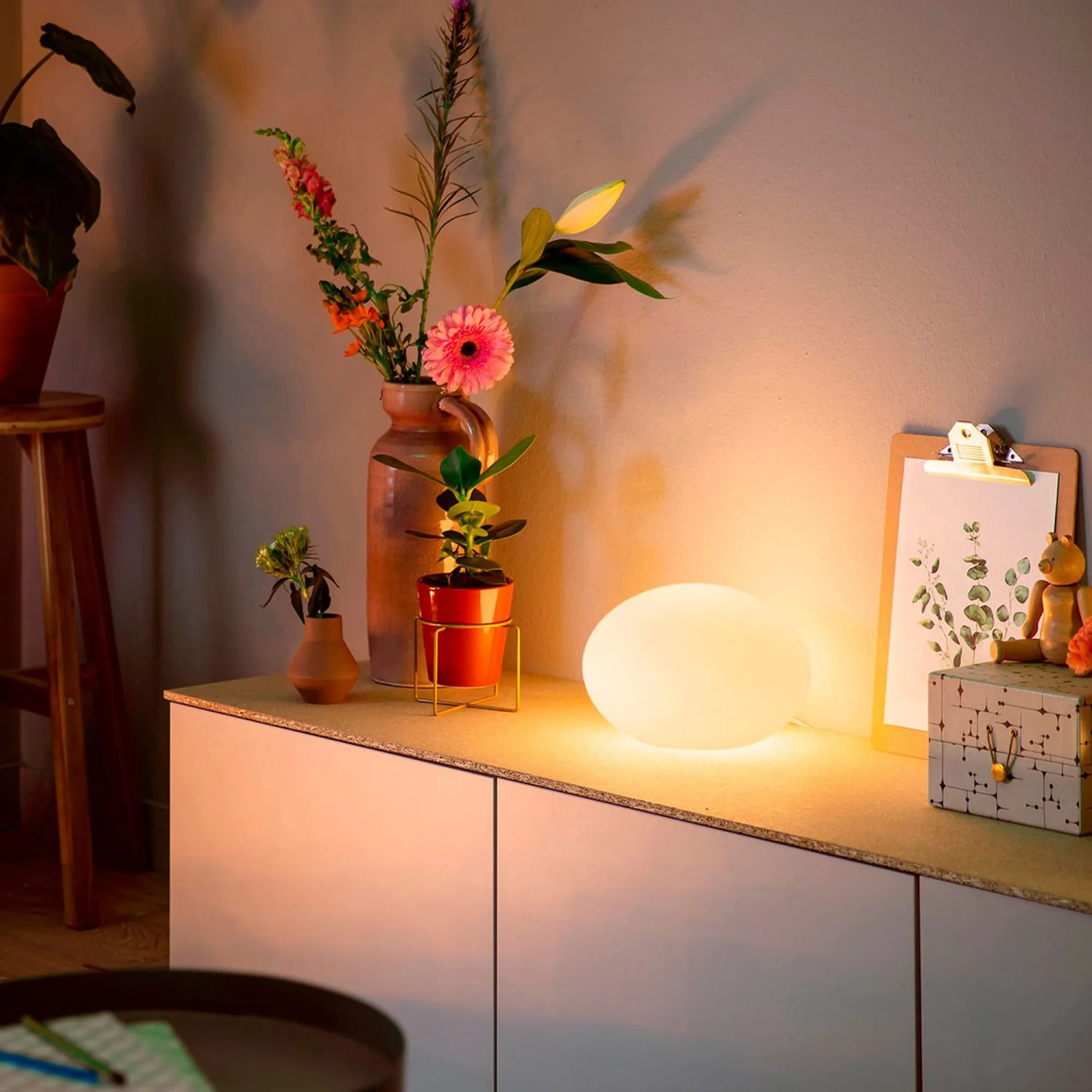 Smarte Philips Hue Tischleuchte Flourish, Weiß- & Farblicht, auf einem Sideboard mit Deko.