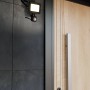 Schwarzer Eglo LED-Wandstrahler Risacca-E mit Sensor an dunkler Hauswand neben einer Haustür.