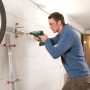 Mann bohrt mit Bosch Akku-Bohrhammer Uneo Maxx in Wand. Reifenhalterung sichtbar.